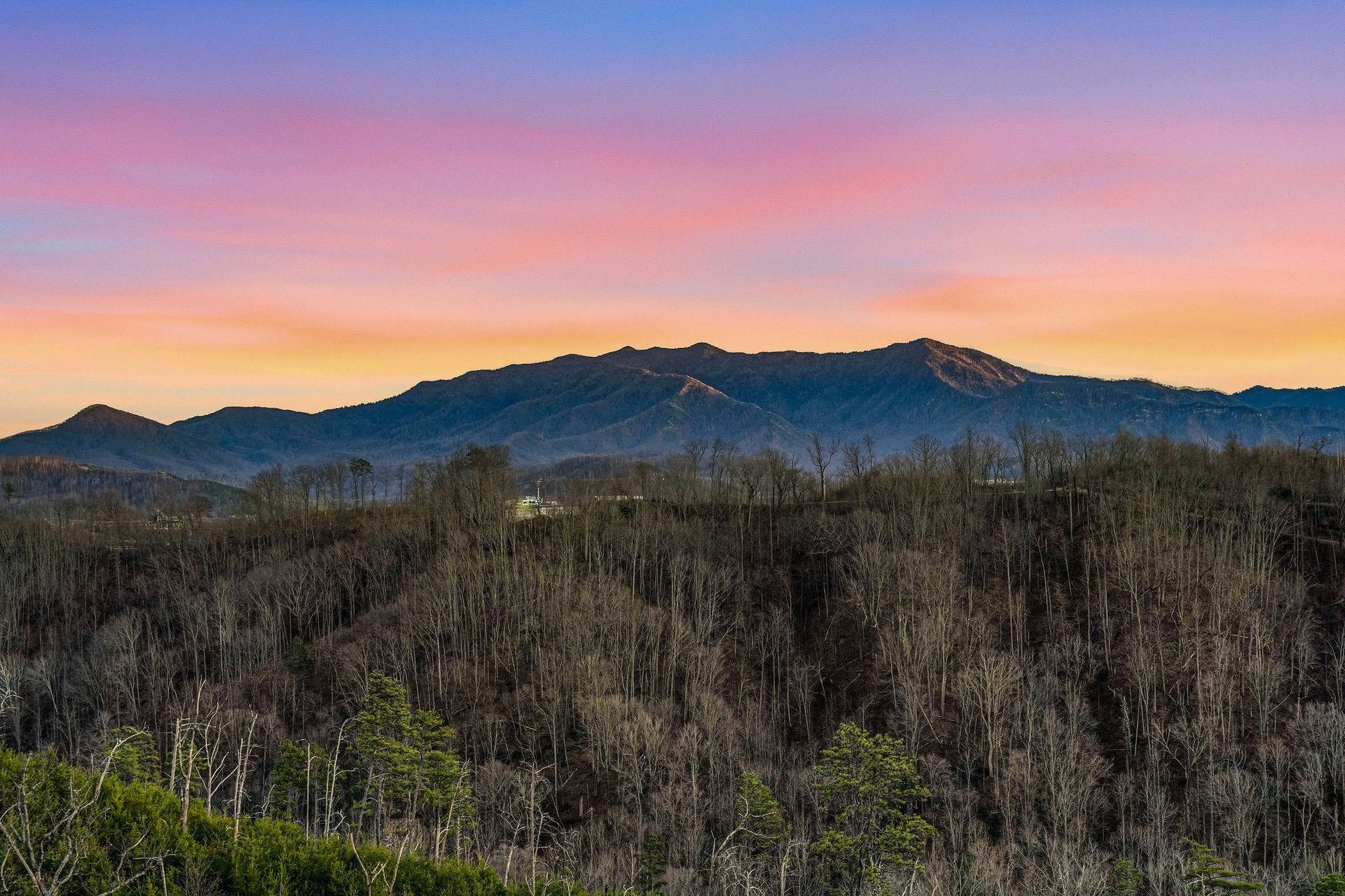 Stunning mountain vista with colorful sunset sky over forested landscape in the surrounding area.