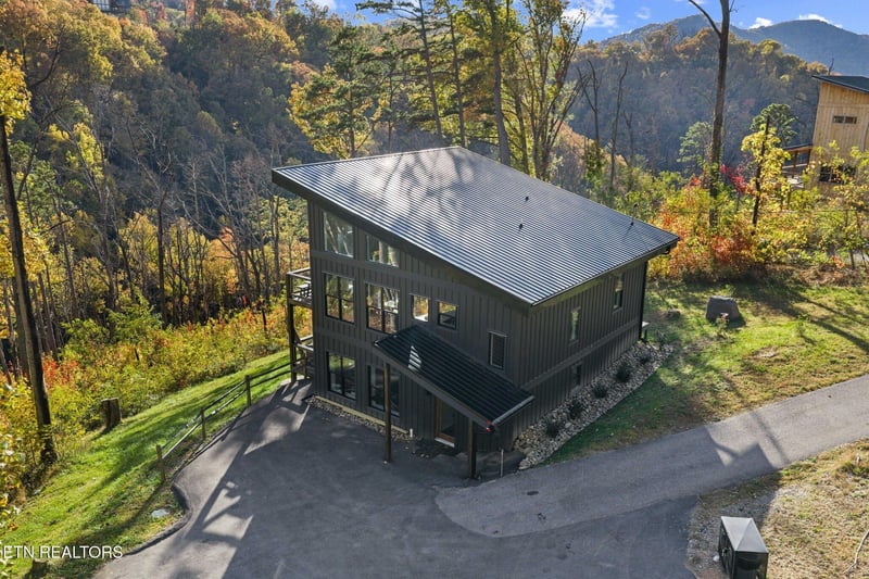 Modern mountain retreat nestled among vibrant autumn foliage, surrounded by towering peaks and serene forest.