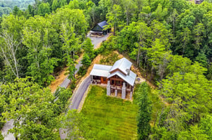 Aerial view of two mountain cabin rentals nestled in a lush forest setting, with paved driveways and private lawns surrounded by dense green woodland.