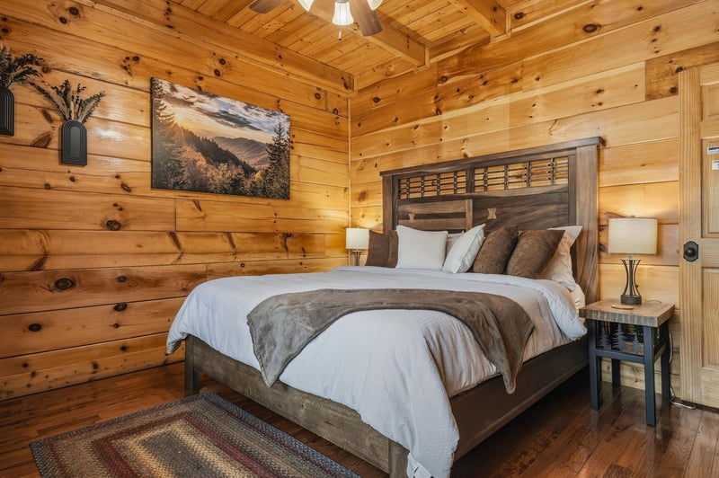 Sink into crisp linens and rustic elegance in your cozy cabin bedroom, where warm wood walls and soft lighting create the perfect retreat after a day exploring the mountains.