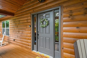 The welcoming entry to your log cabin retreat, adorned with a cheerful wreath and surrounded by warm wood tones and peaceful natural views.