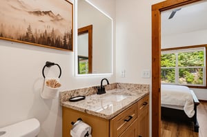 Freshen up in your private bathroom with granite counters and natural woodland charm—lush greenery visible just beyond the bedroom door.