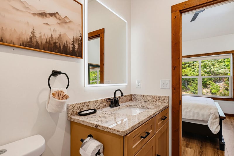 Freshen up in your private bathroom with granite counters and natural woodland charm—lush greenery visible just beyond the bedroom door.