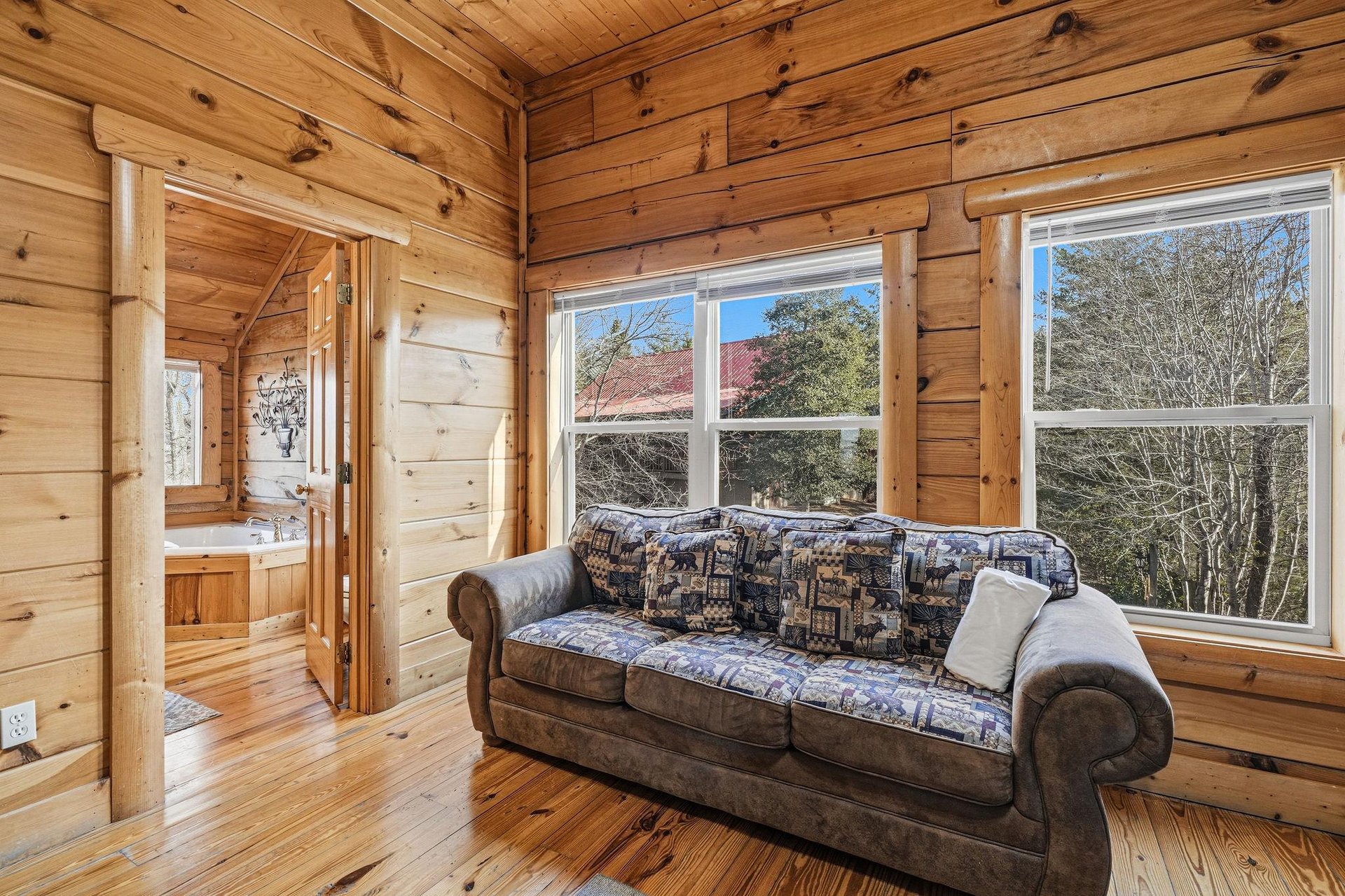 Relax on the plush sofa as warm wood surrounds you, while large windows frame peaceful forest views for your mountain getaway.
