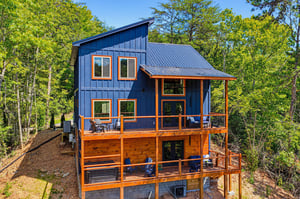 A striking blue and orange modern cabin nestled among lush trees, offering multiple levels of outdoor deck space and a peaceful natural setting.