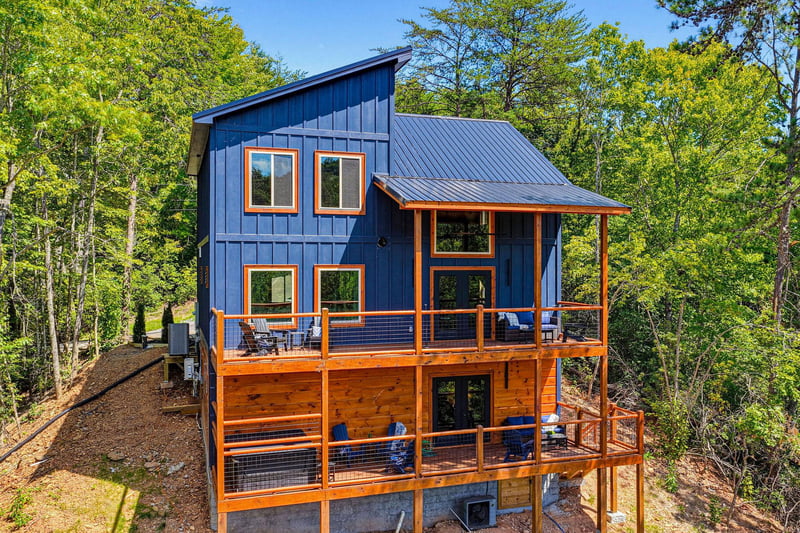 A striking blue and orange modern cabin nestled among lush trees, offering multiple levels of outdoor deck space and a peaceful natural setting.