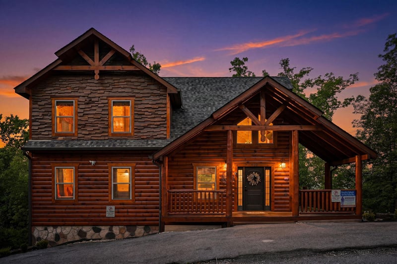 Rustic log cabin nestled in the trees with warm evening lighting and covered porch entry.