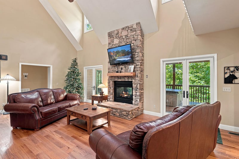 Sink into plush leather sofas and feel the warmth of the crackling stone fireplace in this soaring living room. Your retreat awaits with vaulted ceilings, rich hardwood floors, and French doors openin