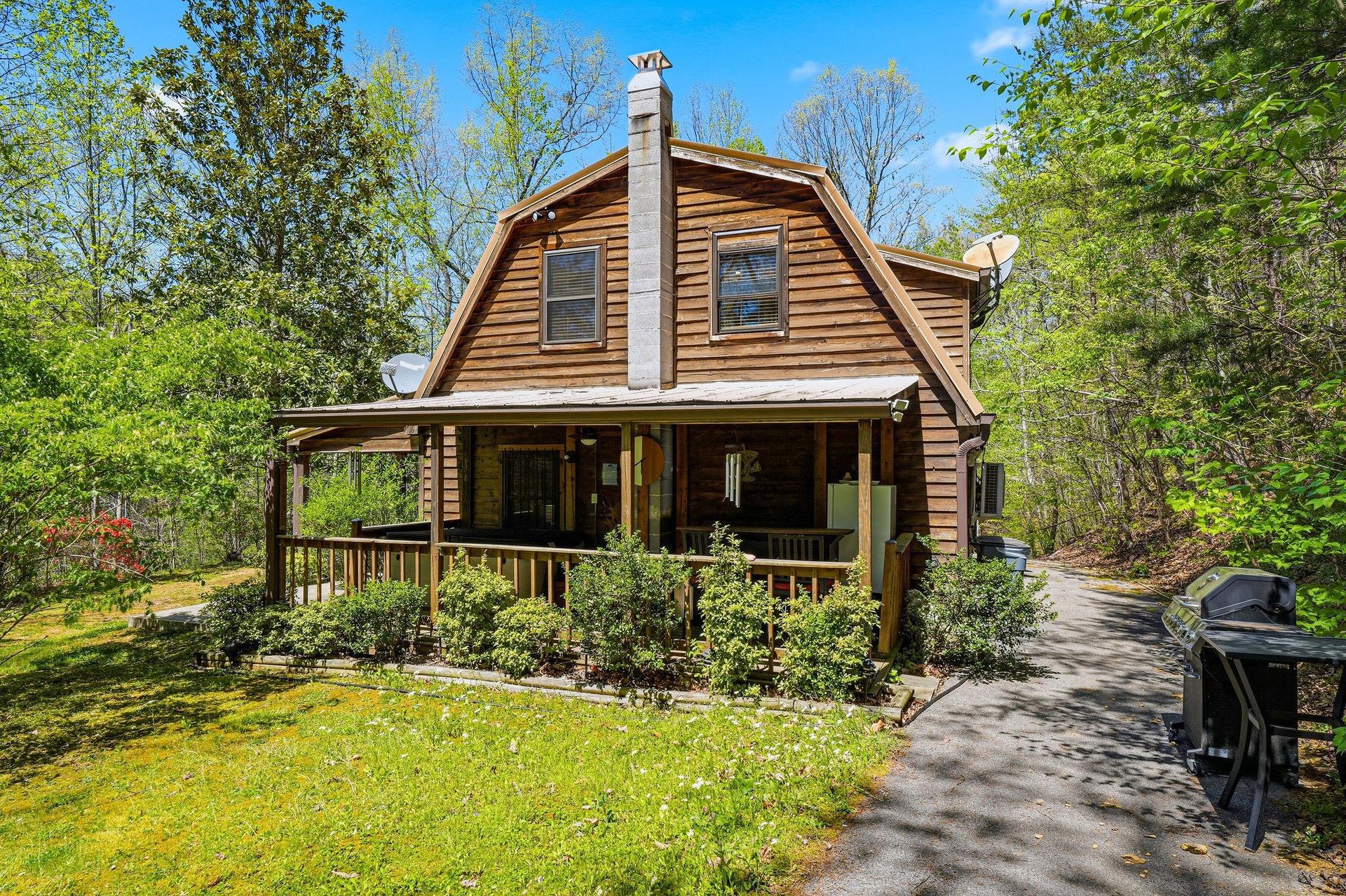 Charming log cabin retreat nestled among towering trees, featuring a welcoming covered porch and peaceful woodland surroundings for your perfect getaway.