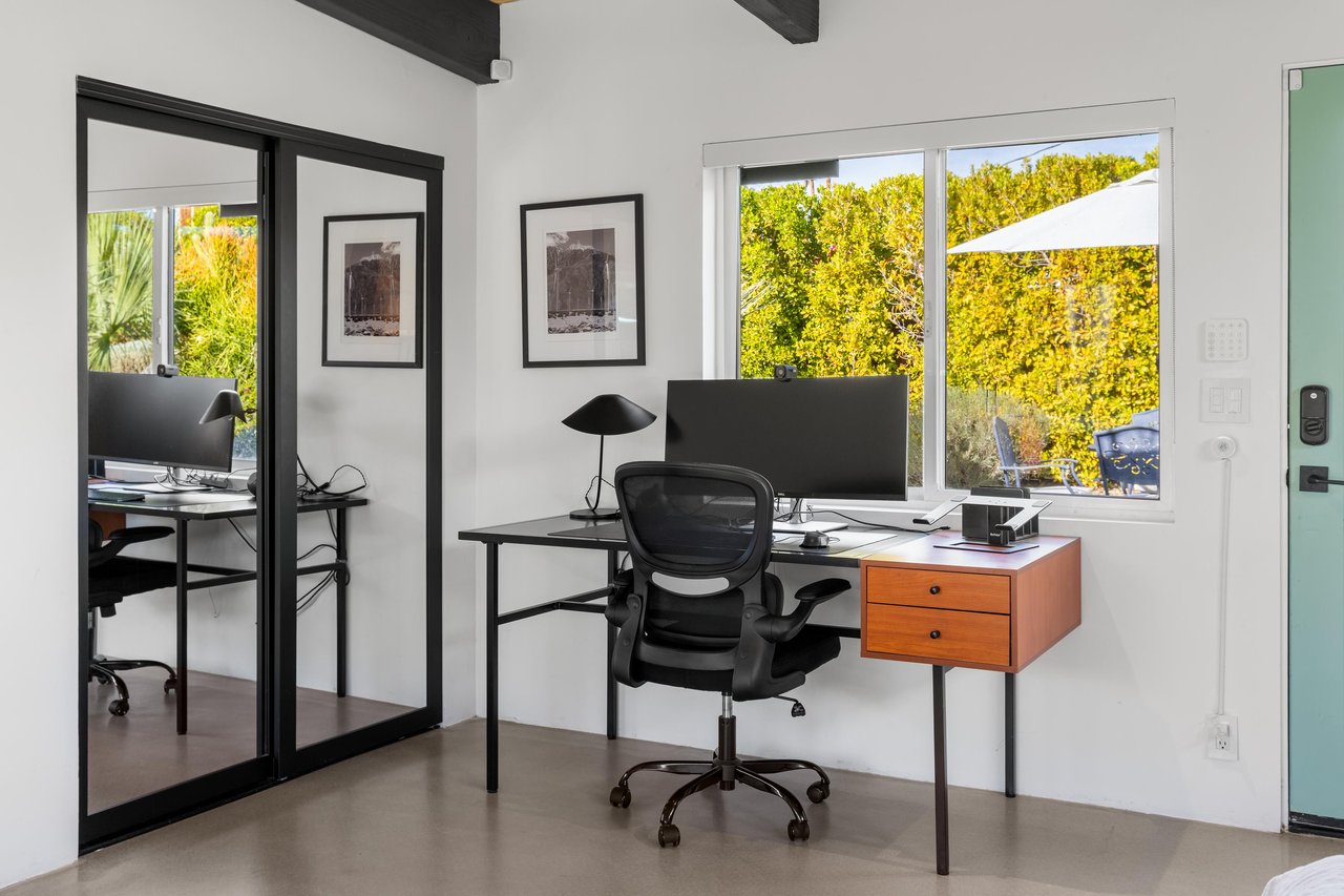 Your dedicated workspace with modern desk, ergonomic chair, and dual monitors overlooks lush greenery through large windows.