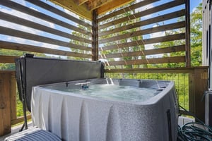 Soak in the warm, bubbling hot tub beneath a wooden pergola as sunlight filters through the slats and fresh greenery frames the horizon.