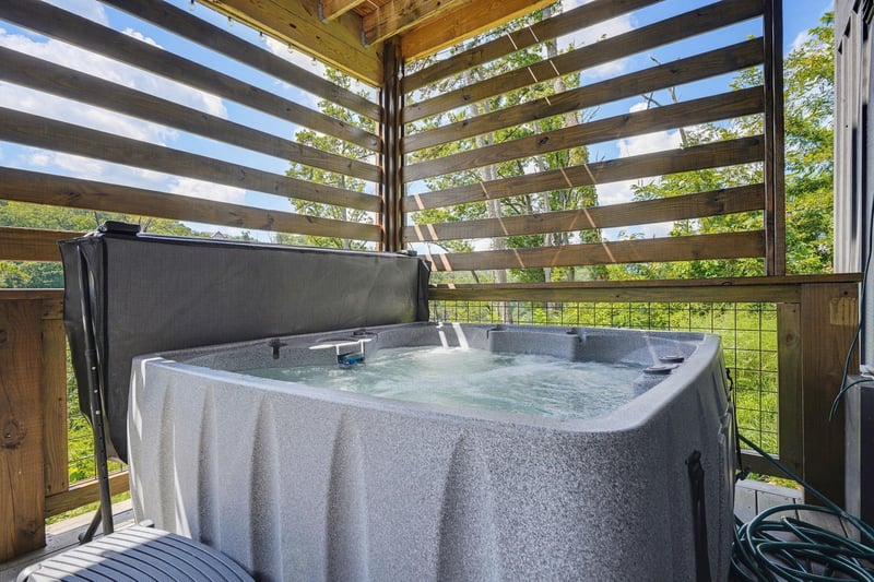 Soak in the warm, bubbling hot tub beneath a wooden pergola as sunlight filters through the slats and fresh greenery frames the horizon.