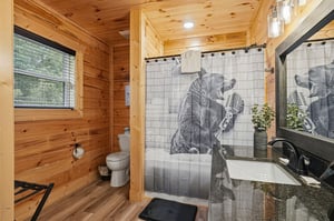 Step into your personal retreat with warm wood walls, a unique bearthemed shower curtain, and a sleek vanity—everything you need to feel refreshed and right at home.