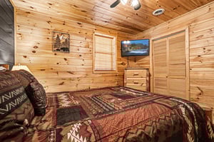 Cozy cabin bedroom with warm pine walls surrounds your restful retreat, complete with rustic charm and modern TV entertainment.