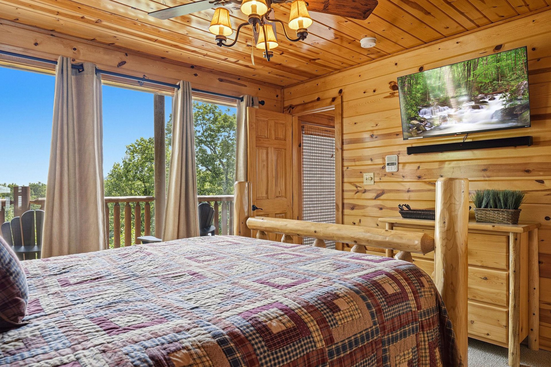 Wake up to beautiful forest views through your private windows. This cozy cabin bedroom features warm wood walls, rustic log furniture, and a plaid quilt for a peaceful mountain retreat.