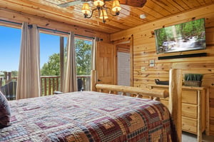 Wake up to beautiful forest views through your private windows. This cozy cabin bedroom features warm wood walls, rustic log furniture, and a plaid quilt for a peaceful mountain retreat.