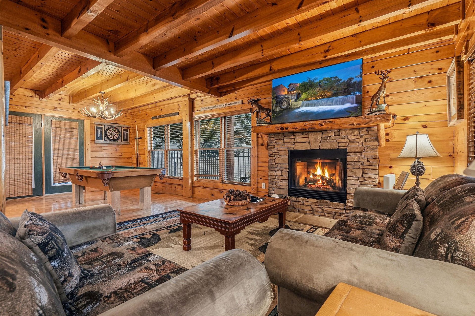 Relax in your cozy living room with soaring woodbeam ceilings, a crackling stone fireplace, plush seating, and a pool table—perfect for unwinding after mountain adventures.
