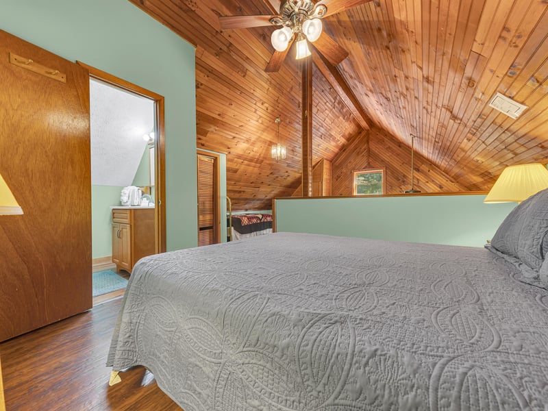 Cozy attic bedroom with rustic wood beams where youll sleep peacefully under soaring ceilings and warm lighting.