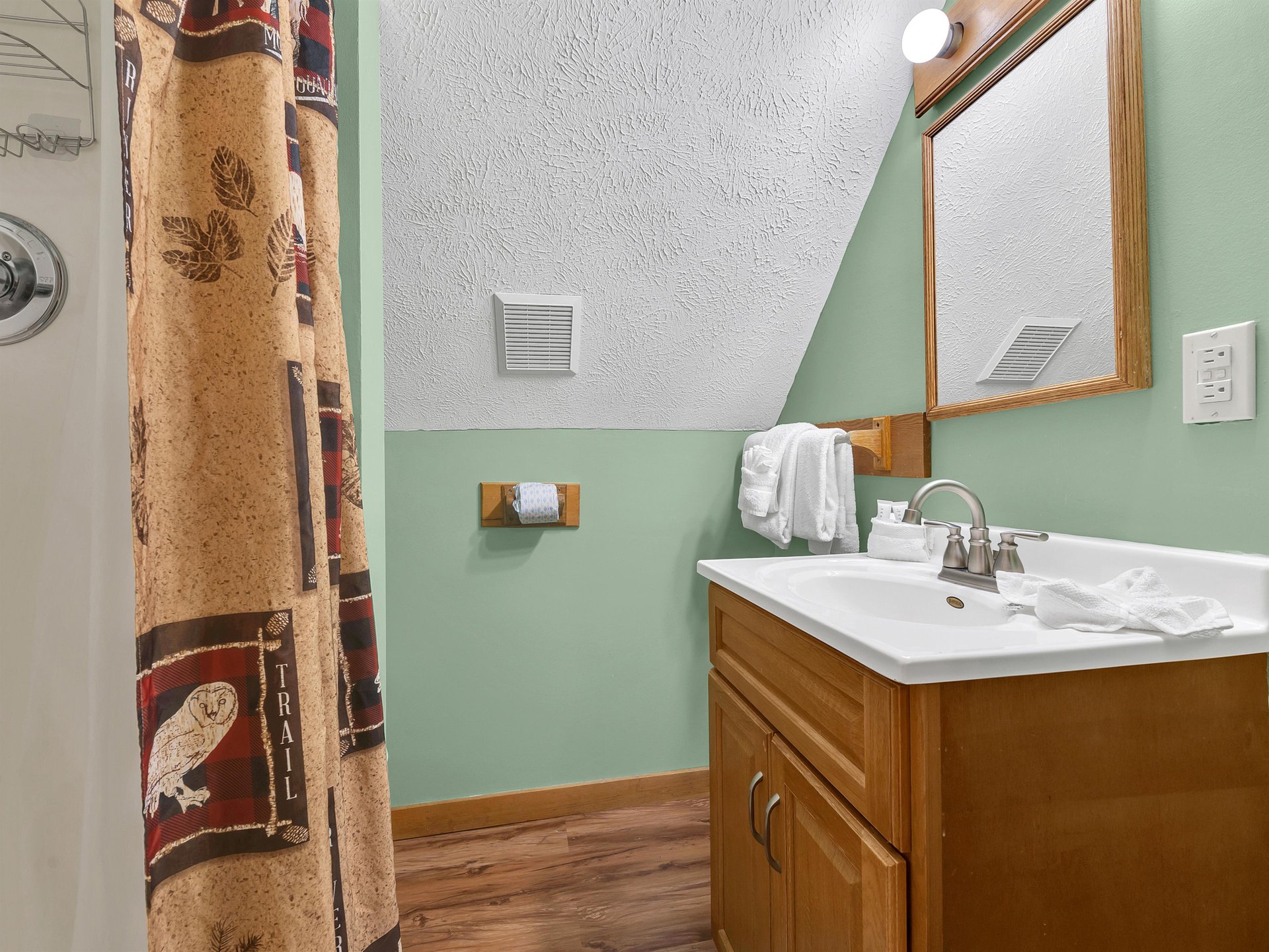 Fresh towels await in your cozy bathroom with warm mint walls, rich wood vanity, and rustic charm.