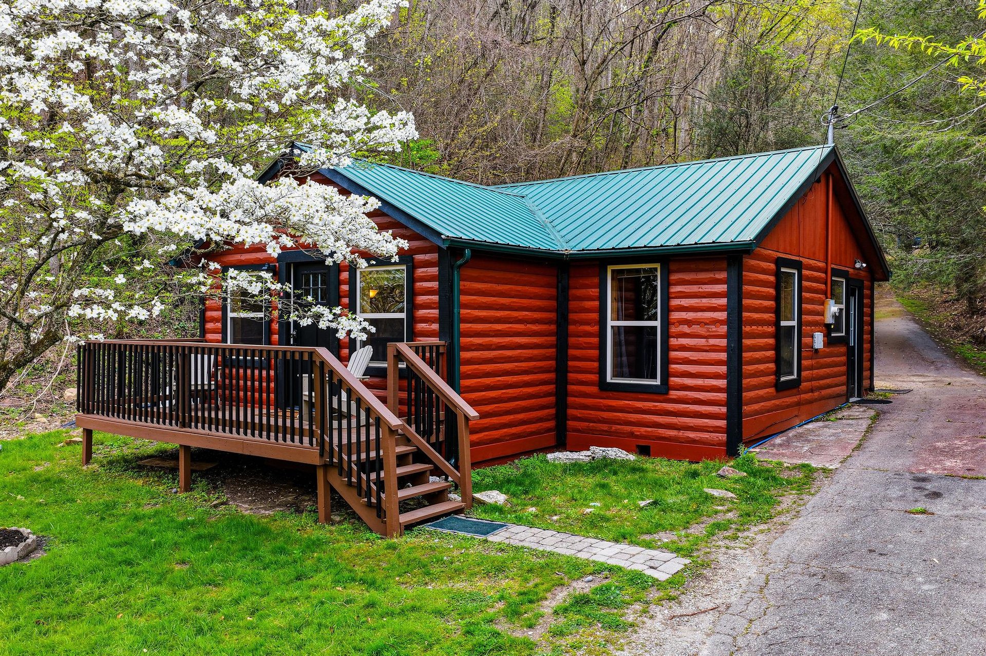 Charming log cabin nestled among blooming spring trees, featuring a welcoming deck where you can relax and enjoy the peaceful natural surroundings.