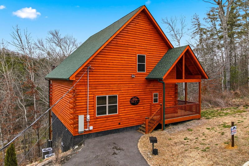 This charming log cabin features warm wood siding and a welcoming covered porch, nestled among trees for a peaceful mountain getaway.