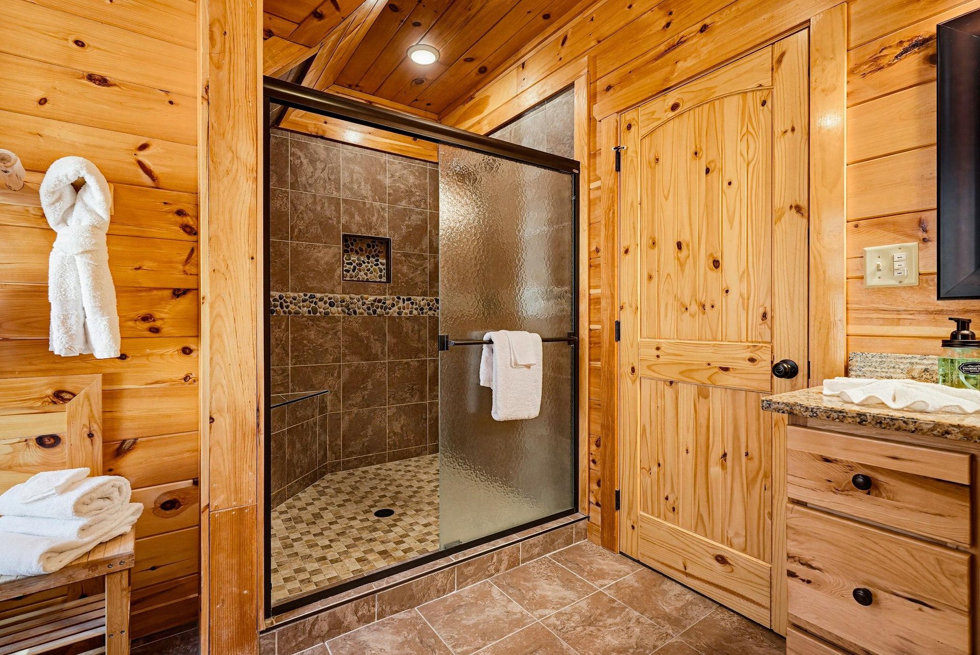 Warm wood tones surround your private bathroom featuring a beautifully tiled walkin shower with classic earthtone finishes. Fresh towels await, ready for your mountain retreat.