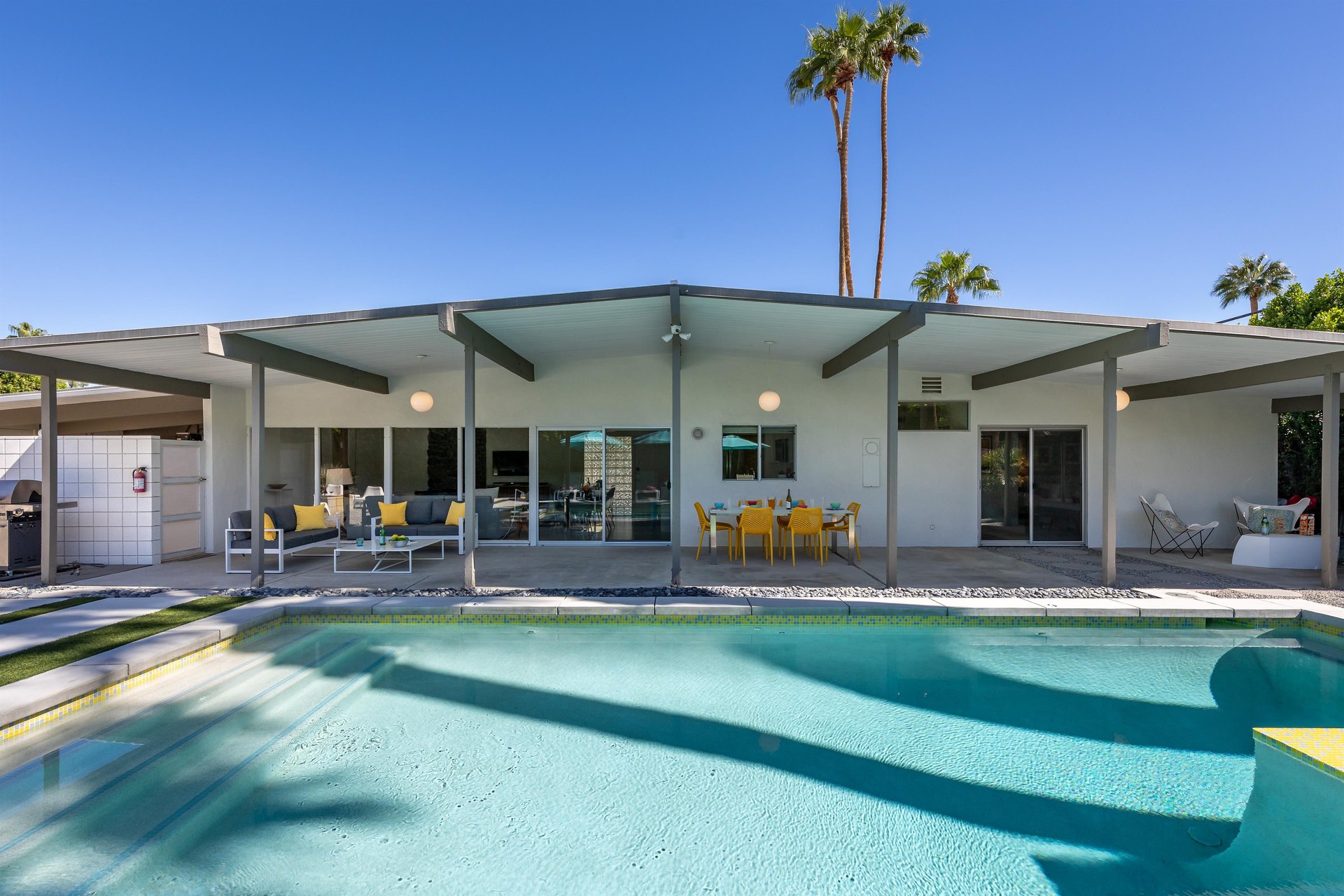 Modern desert oasis featuring a pristine swimming pool and covered outdoor living spaces under palm trees.