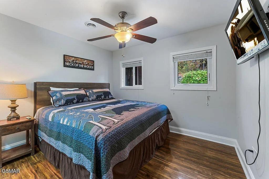 Rest peacefully in this cozy bedroom with rustic wood furnishings, ceiling fan, and windows overlooking lush greenery.