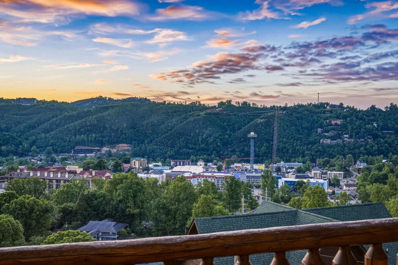 Hillside town nestled among lush forests and valleys, viewed at sunset with softly illuminated buildings and a dramatic sky overhead.