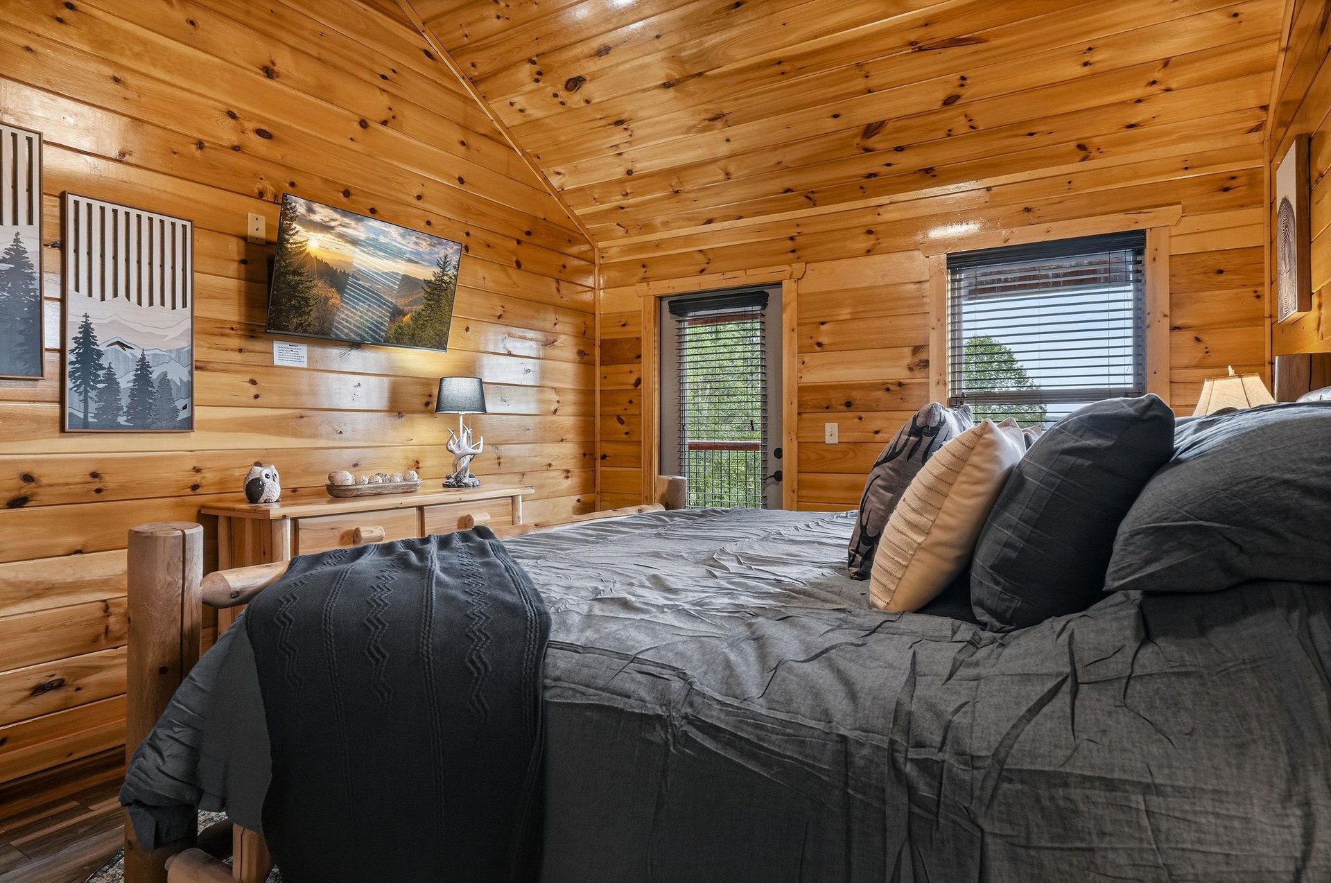 Sink into cozy linens surrounded by warm wood tones, where morning light filters through your private balcony door and mountain art sets the scene for a peaceful retreat.