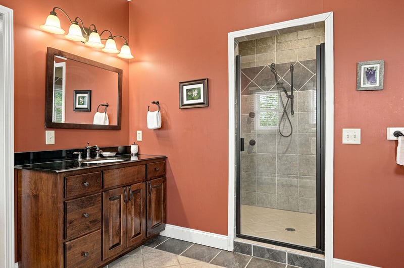 Step into your private bathroom featuring warm coral walls, a polished vanity with black granite countertops, and a spacious walkin shower with elegant tile work—your personal retreat awaits.