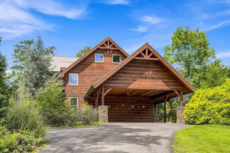 The lodge exterior showcases rustic wooden siding and a covered carport, nestled among lush greenery under a bright blue sky.