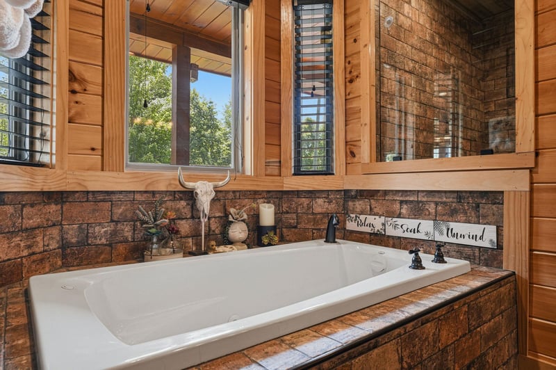 Slip into your private soaking tub surrounded by rustic brick and warm wood accents, with peaceful treetop views framing your relaxation.