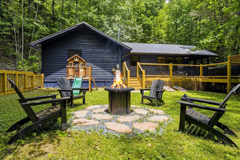 A charming forest retreat with a cozy fire pit surrounded by Adirondack chairs, perfect for evening gatherings under the trees. The spacious deck and playhouse add fun for all ages.