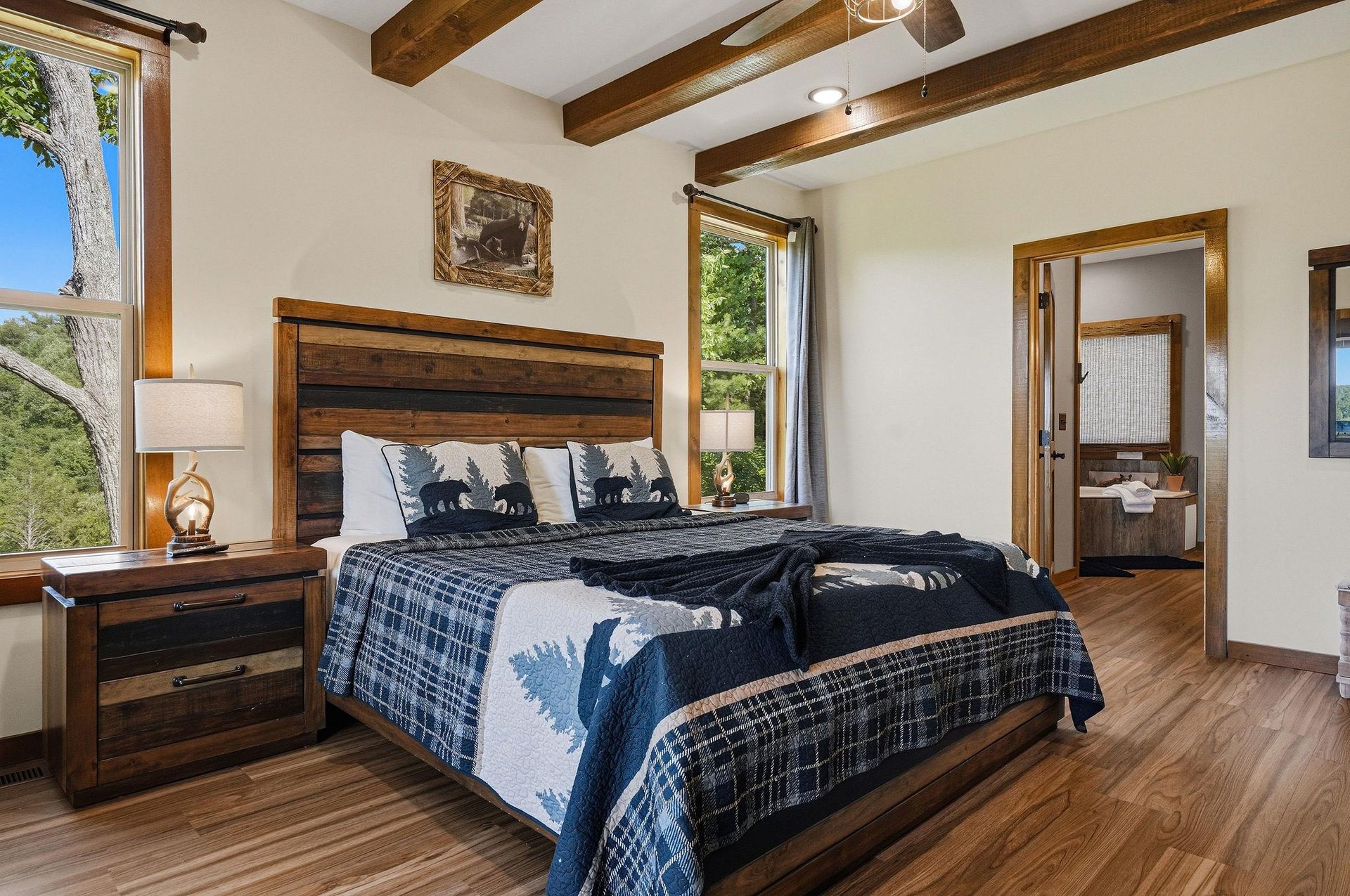 Drift off beneath rustic wood beams in this inviting bedroom, where large windows frame peaceful mountain views and a cozy ensuite bath awaits your morning routine.