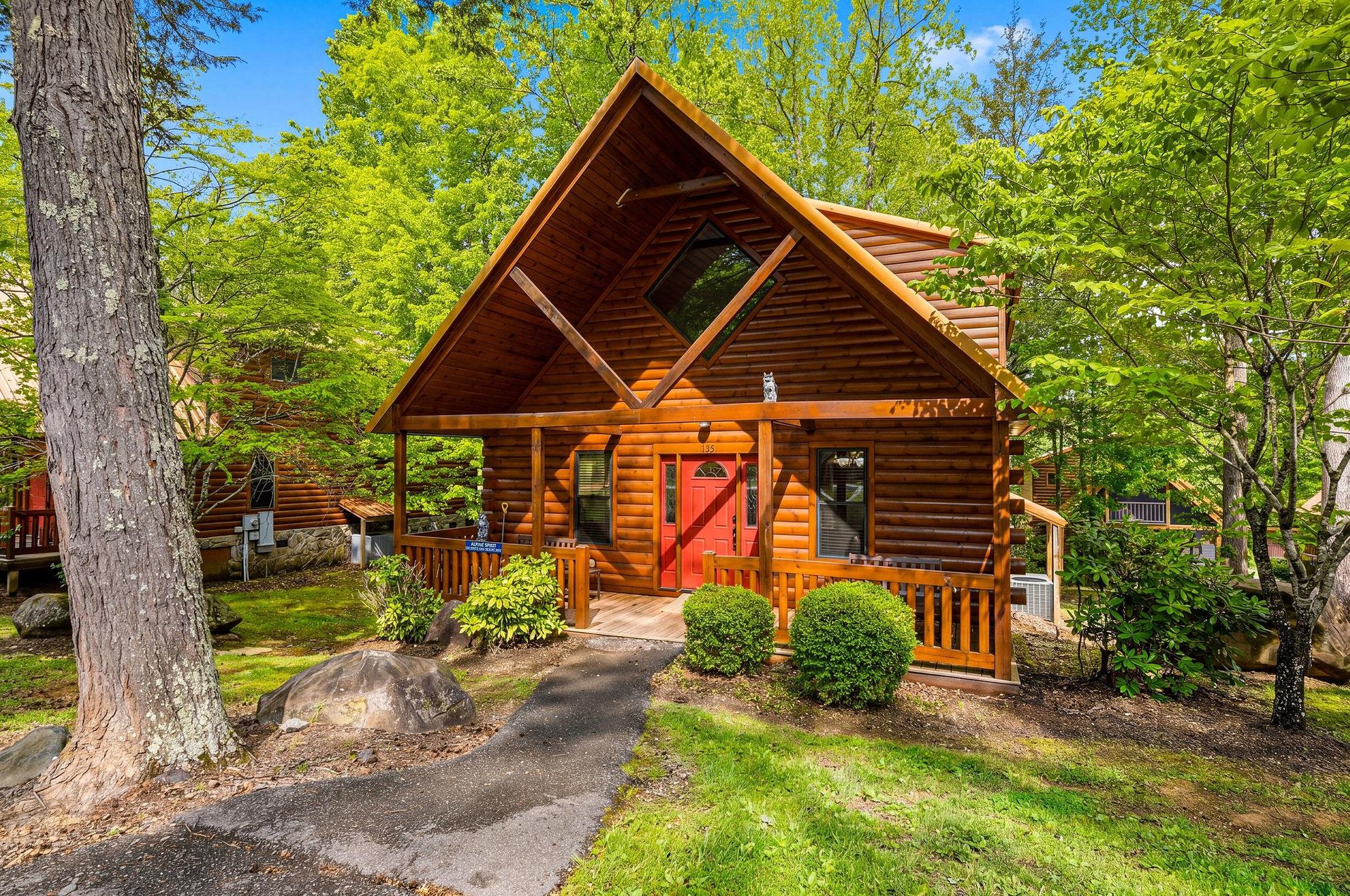 Charming log cabin nestled among towering trees with a welcoming covered porch and bright red door.