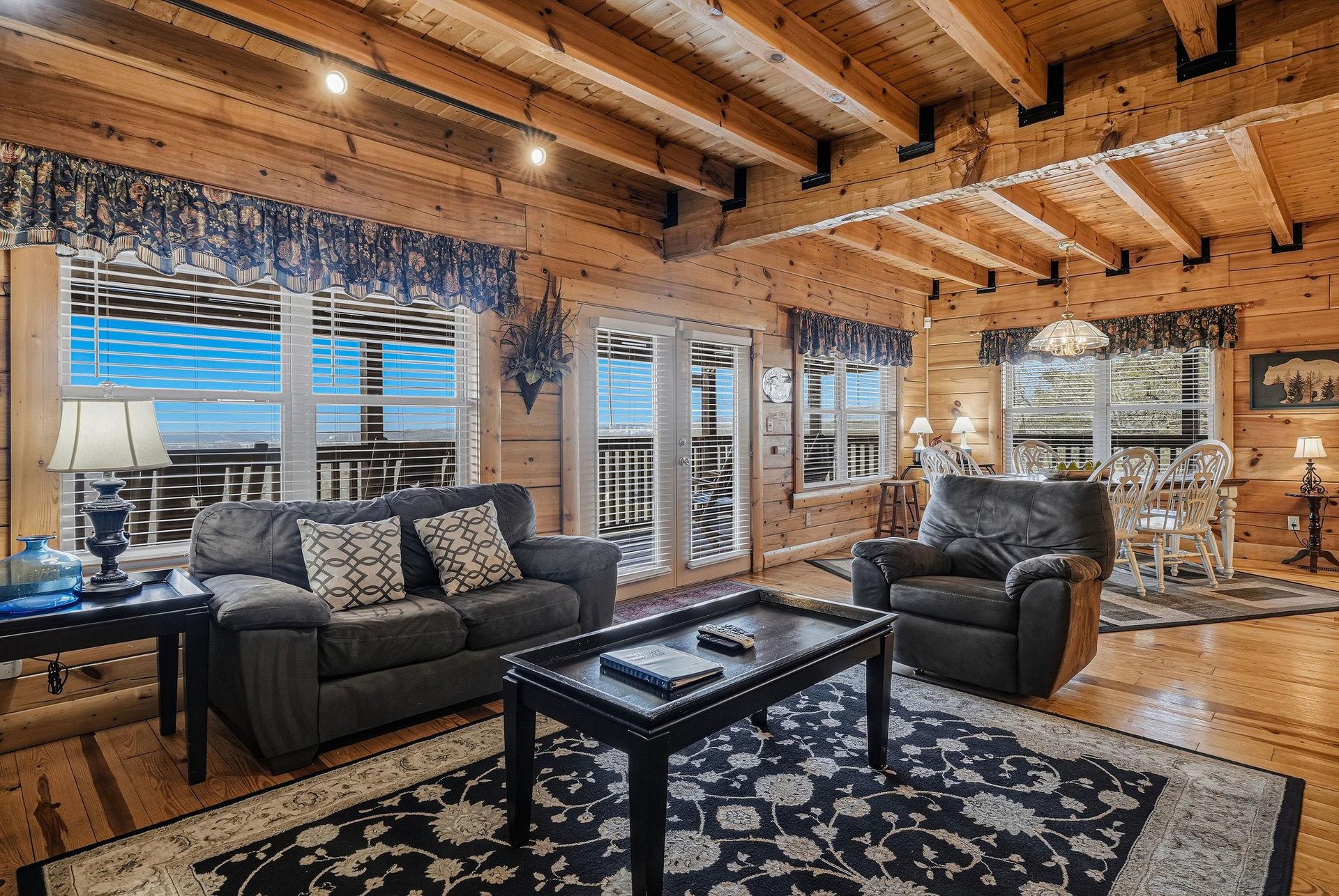 Unwind in your rustic living space with exposed beams, cozy leather seating, and stunning lake views through expansive windows.
