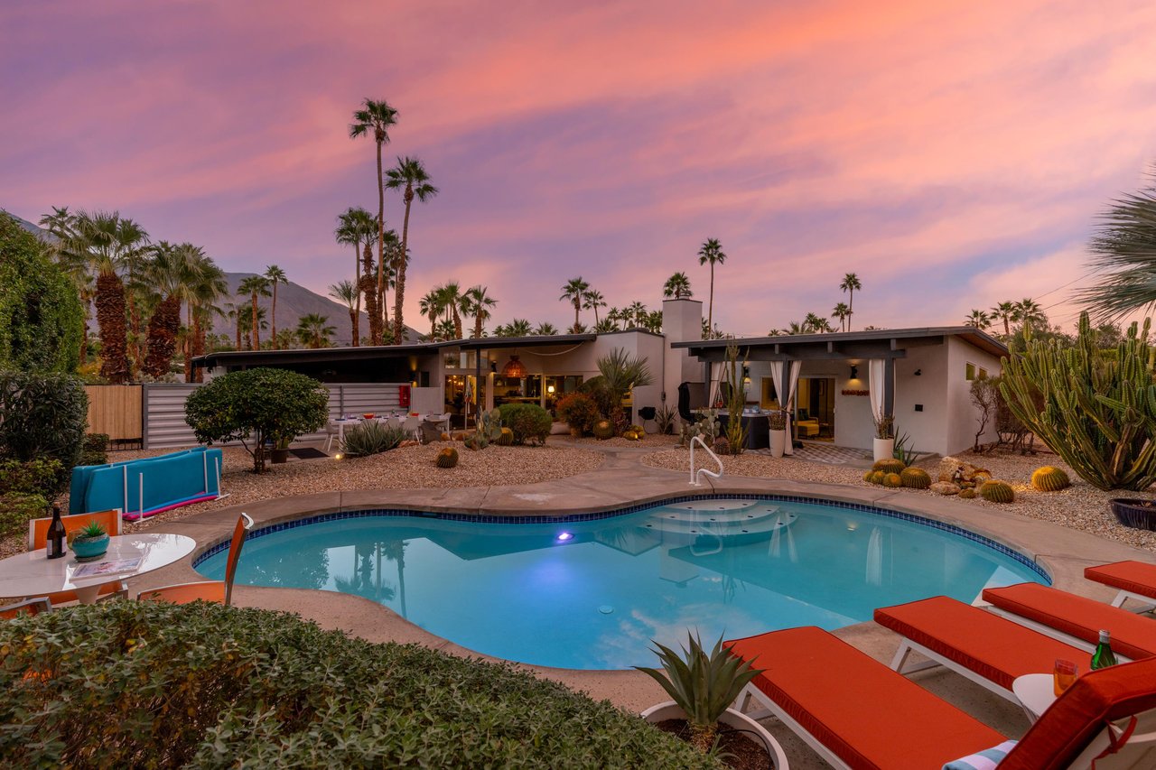 Midcentury modern retreat showcasing sparkling pool and desert landscaping beneath vibrant sunset skies.