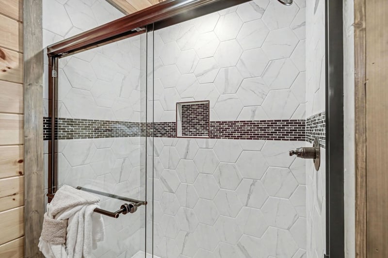 Step into your beautifully tiled shower featuring elegant hexagonal marble with decorative mosaic accents and gleaming fixtures.