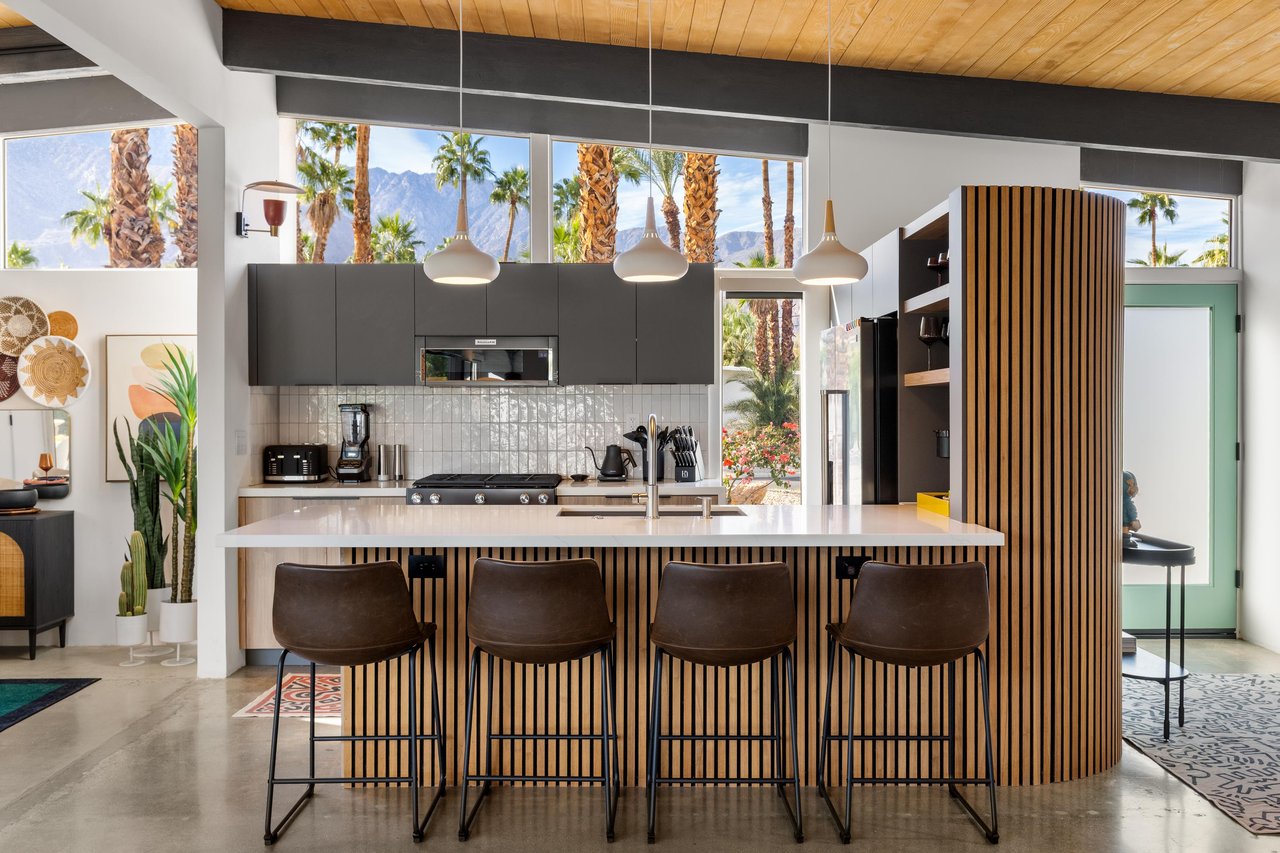 Your sleek modern kitchen features premium appliances and a stunning breakfast bar, all framed by desert palms through floortoceiling windows.