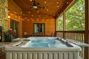 Soak in your private hot tub on this covered porch, surrounded by lush forest views and twinkling lights for cozy evenings under the warm wooden ceiling.