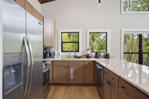 Your fully equipped kitchen features stainless steel appliances, ample counter space, and bright windows framing peaceful tree views—perfect for preparing meals in natural light.