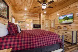 Unwind in your cozy cabin bedroom with rustic wood walls, plaid bedding, and mountain views on the flatscreen TV for ultimate relaxation.