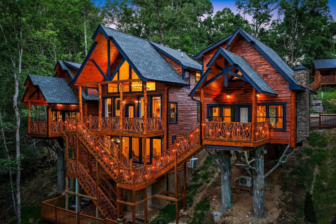 A stunning treehousestyle cabin nestled in the forest, featuring expansive wooden decks and rustic architectural details. The property is surrounded by lush greenery and photographed during the twili