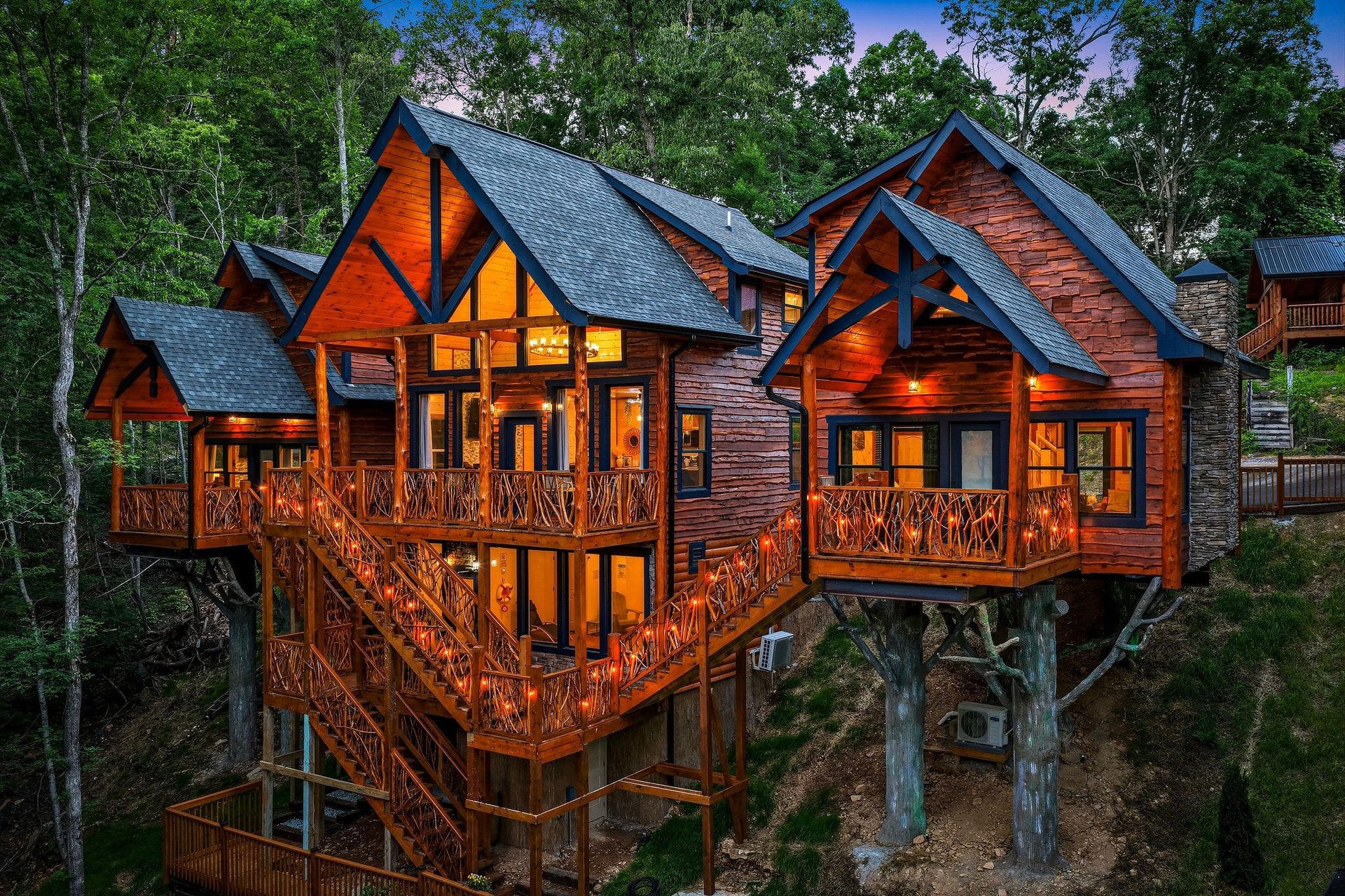 A stunning treehousestyle cabin nestled in the forest, featuring expansive wooden decks and rustic architectural details. The property is surrounded by lush greenery and photographed during the twili