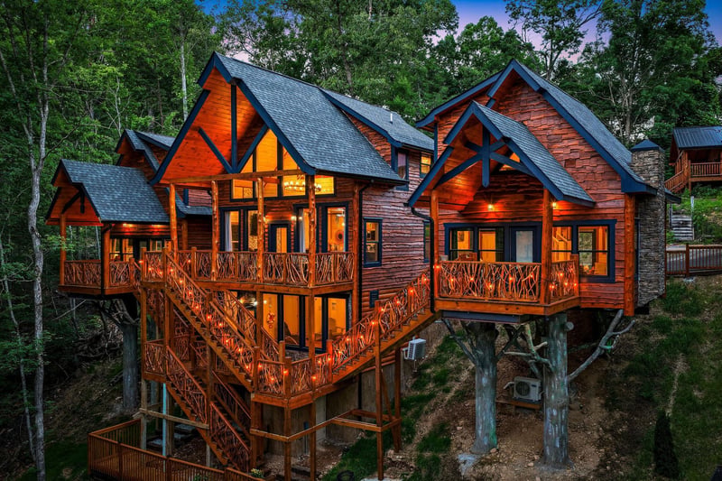 A stunning treehousestyle cabin nestled in the forest, featuring expansive wooden decks and rustic architectural details. The property is surrounded by lush greenery and photographed during the twili