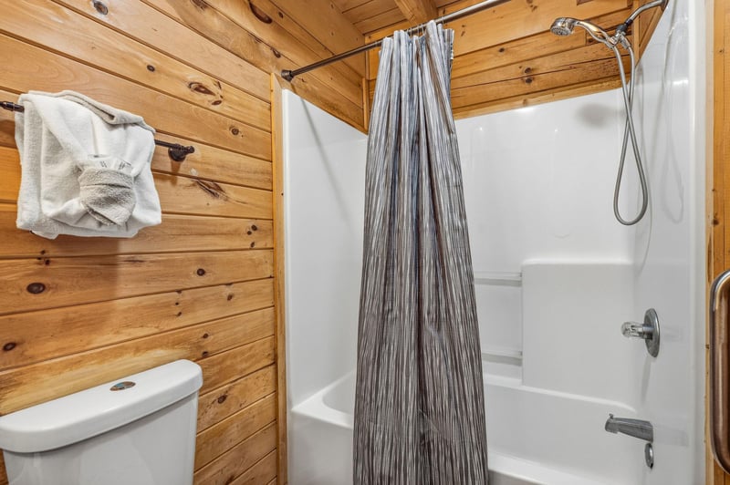 Step into your rusticmodern bathroom featuring warm wood walls, a refreshing showertub combo, and fresh towels ready for your mountain getaway.