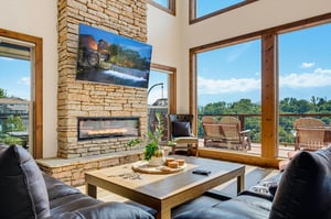 Relax in your bright living room where a soaring stone fireplace and floortoceiling windows frame stunning views of lush greenery and open skies.