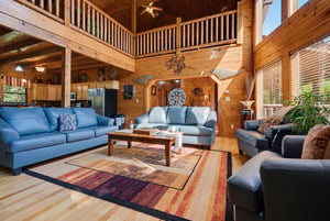 Stunning cathedral ceilings and handsome wood beams frame this inviting openplan living space, where you can unwind on plush seating and soak in the cabins warm, rustic charm.