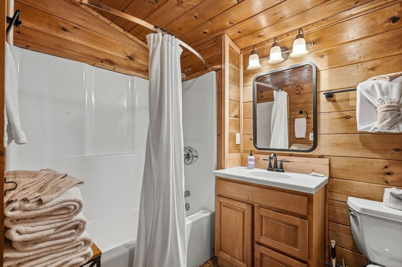Warm woodpaneled bathroom features everything you need  spacious shower, vanity, and cozy cabin atmosphere for ultimate relaxation.